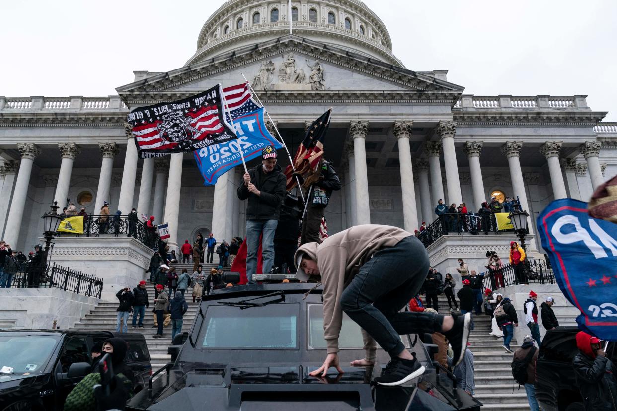 Supporters of then-President Donald Trump, some carrying American flags and Trump banners, gather on the steps of the U.S. Capitol.