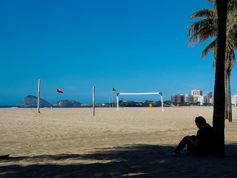 A girl sits under a tree on an empty Copacabana Beach during a sunny Saturday morning on March 28, 2020 in Rio de Janeiro, Brazil.