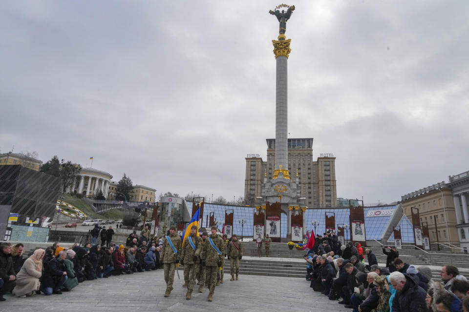 People stand kneeling as the Ukrainian servicemen carry a coffin of their comrade Oleh Yurchenko killed in a battlefield with Russian forces in Donetsk region during a commemoration ceremony in Independence Square in Kyiv, Ukraine, Sunday, Jan. 8, 2023. (AP Photo/Efrem Lukatsky)