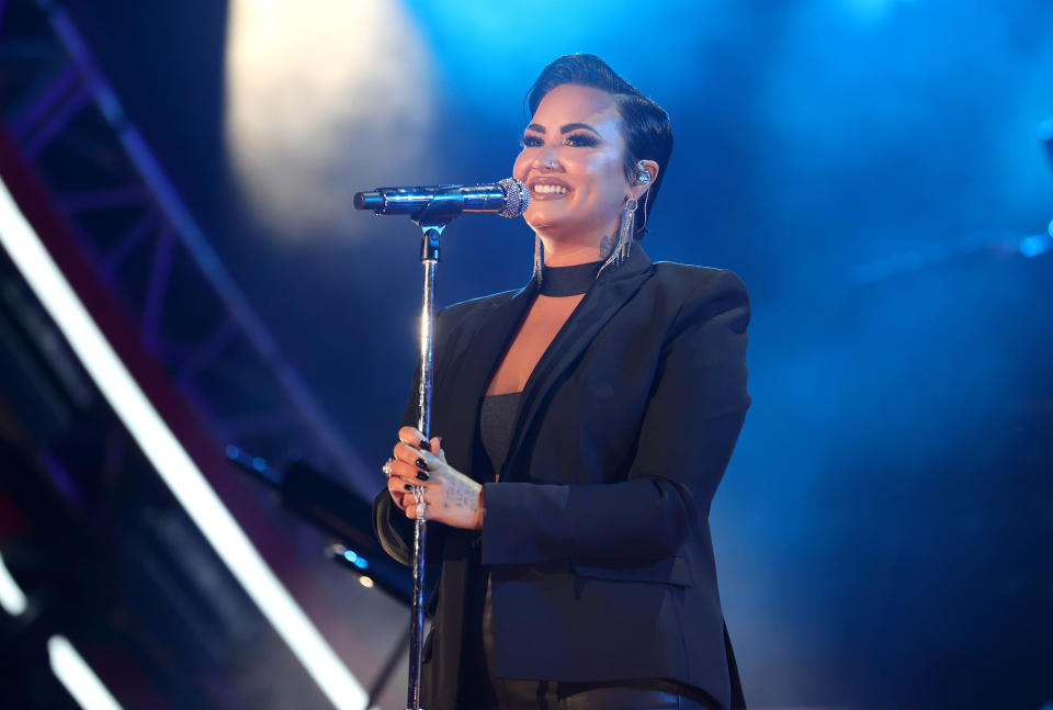 Demi Lovato smiling in front of a microphone while performing on stage