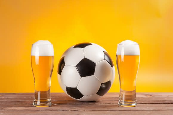 A soccer ball sits between two pints of beer.
