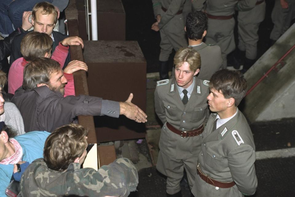 East German border policemen, right, refuse to shake hands with a Berliner who stretches out his hand over the border fence at the eastern site nearby Checkpoint Charlie border crossing point on November 10, 1989, after the borders were opened according to the announcement by the East German government.