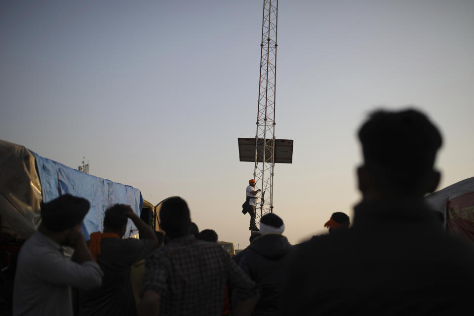 A farmer attempts to climb a tower, as fellow farmers watch him as they attempt to move towards Delhi, at the border between Delhi and Haryana state, Friday, Nov. 27, 2020. Thousands of agitating farmers in India faced tear gas and baton charge from police on Friday after they resumed their march to the capital against new farming laws that they fear will give more power to corporations and reduce their earnings. While trying to march towards New Delhi, the farmers, using their tractors, cleared concrete blockades, walls of shipping containers and horizontally parked trucks after police had set them up as barricades and dug trenches on highways to block roads leading to the capital. (AP Photo/Altaf Qadri)