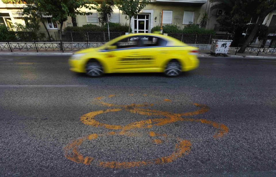 A taxi drives by fading Olympic rings which mark the Olympic Traffic Lane on an avenue leading to the Athens 2004 Olympic Complex in Athens