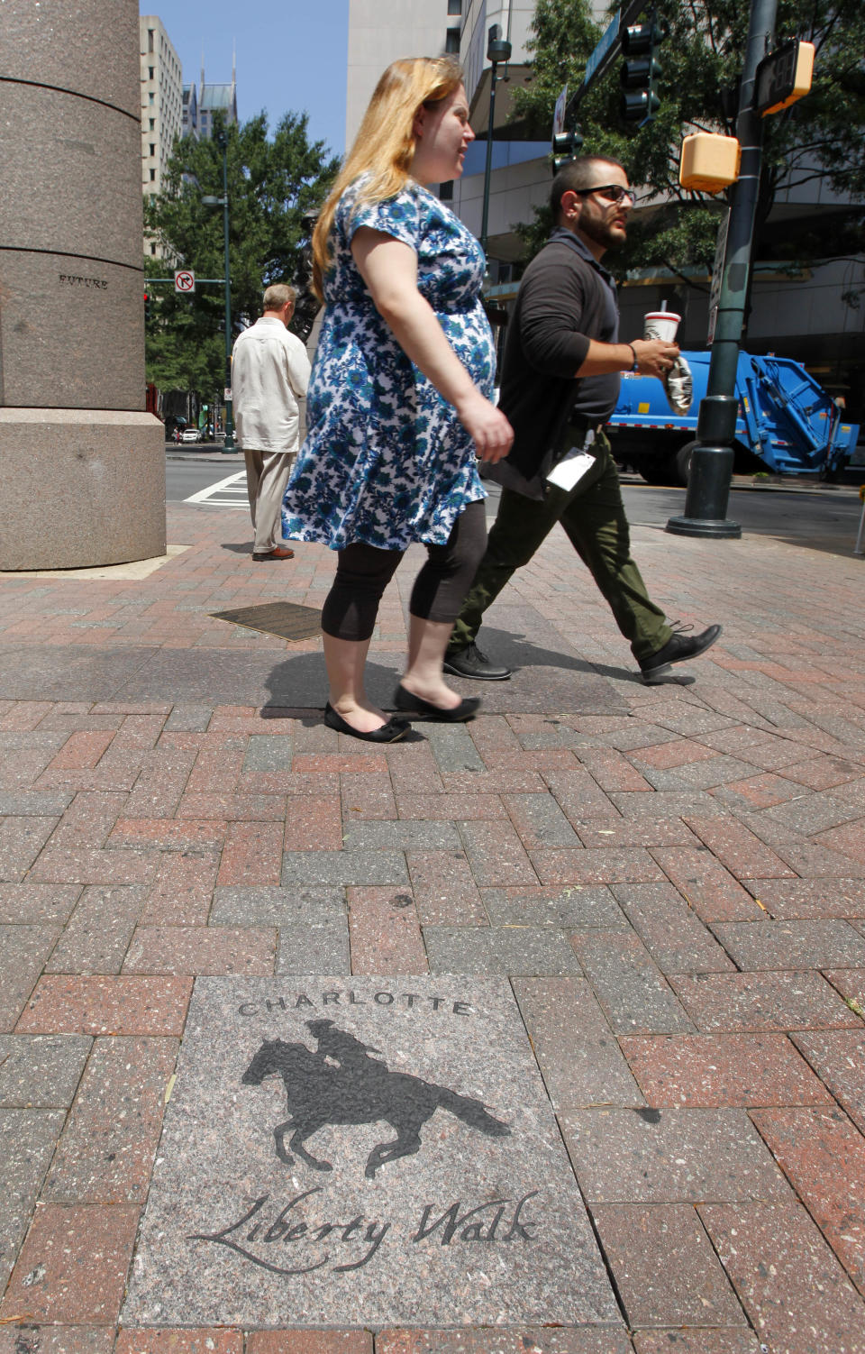 This July 17, 2012 photo shows pedestrians walking past a marker for a self-guided tour in downtown Charlotte, N.C. Several self-guided walking tours cover the NASCAR Hall of Fame, the Bechtler, Mint and Levine museums and a stop at Settlers' Cemetery, where town founder and Revolutionary War hero Thomas Polk is buried. (AP Photo/Chuck Burton)