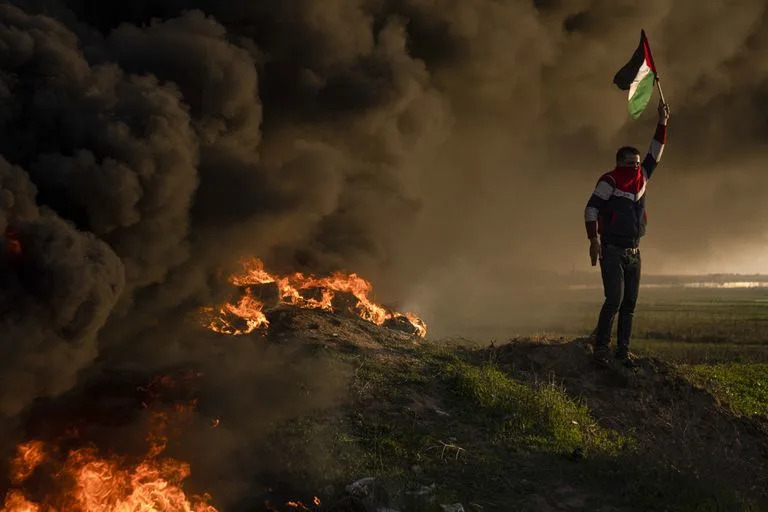 Palestinos queman neumáticos y ondean la bandera nacional durante una protesta contra una incursión militar israelí en la ciudad cisjordana de Yenín, junto a la valla fronteriza con Israel, en el este de la ciudad de Gaza, el jueves 26 de enero de 2023.