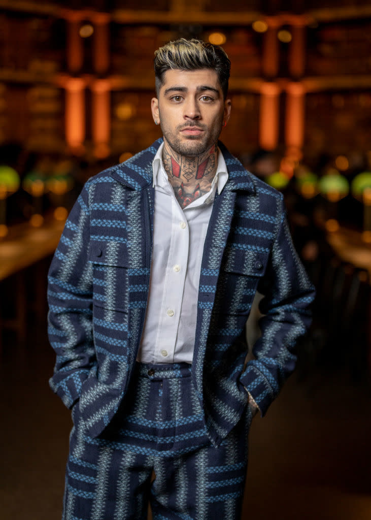 Zayn in patterned suit and open-collar shirt, standing with hands in pockets, blurred background