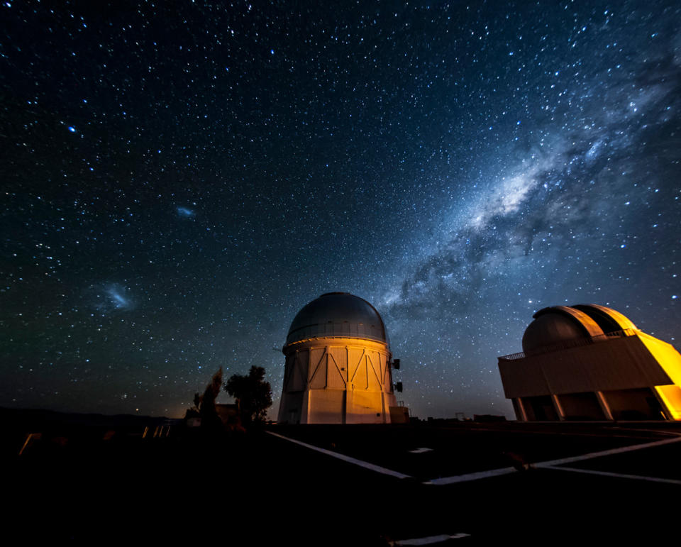 two dimly lit observatories sit like stunted domes beneath a vibrant night sky and a swath of blue-tinted milky way.