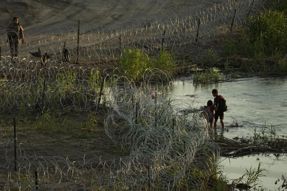 A Texas state trooper watches as young migrants walk along concertina wire on the banks of the Rio Grande as they try to enter the U.S. from Mexico in Eagle Pass, Texas, Thursday, July 6, 2023. Texas Republican Gov. Greg Abbott has escalated measures to keep migrants from entering the U.S. He's pushing legal boundaries along the border with Mexico to install razor wire, deploy massive buoys on the Rio Grande and bulldozing border islands in the river. (AP Photo/Eric Gay)