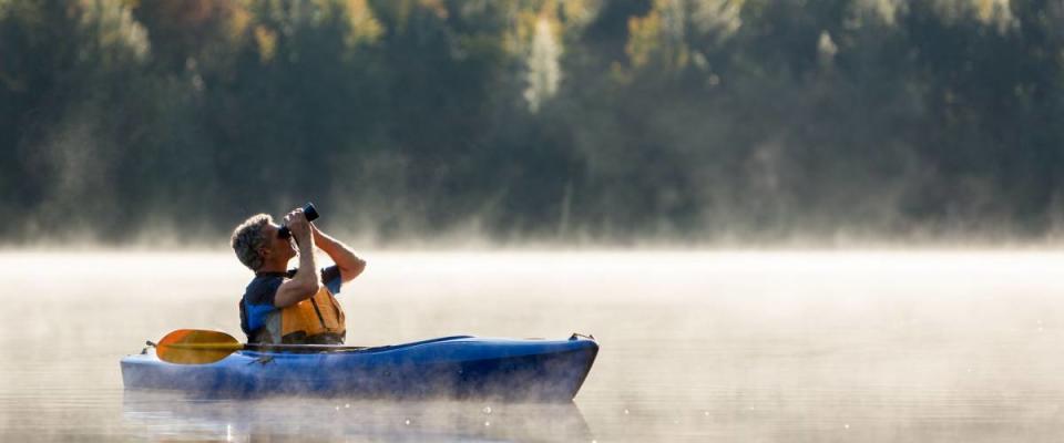 Senior man solo traveller birdwatching from kayak in morning fog