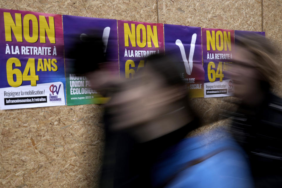 Passers-by walk past posters opposing to retirement at age 64, Tuesday, March 7, 2023 in Paris. Demonstrators were marching across France on Tuesday in a new round of protests and strikes against the government's plan to raise the retirement age to 64, in what unions hope to be their biggest show of force against the proposal. (AP Photo/Christophe Ena)
