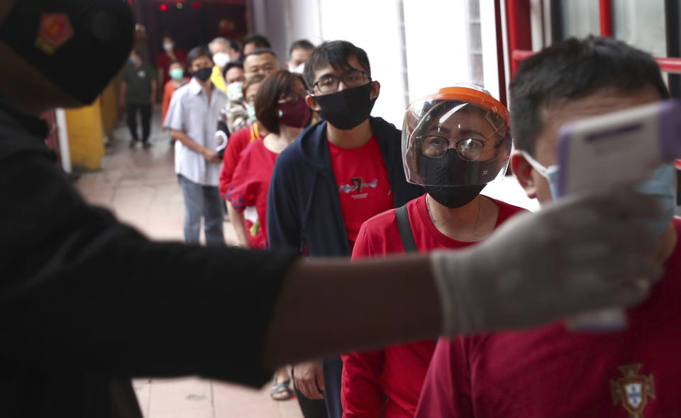 A security guard checks the temperature of worshippers at the entrance of a temple amid concerns of coronavirus outbreak during the Lunar New Year of the Ox celebrations in the China Town area of Jakarta, Indonesia, Friday, Feb. 12, 2021. (AP Photo/Tatan Syuflana)