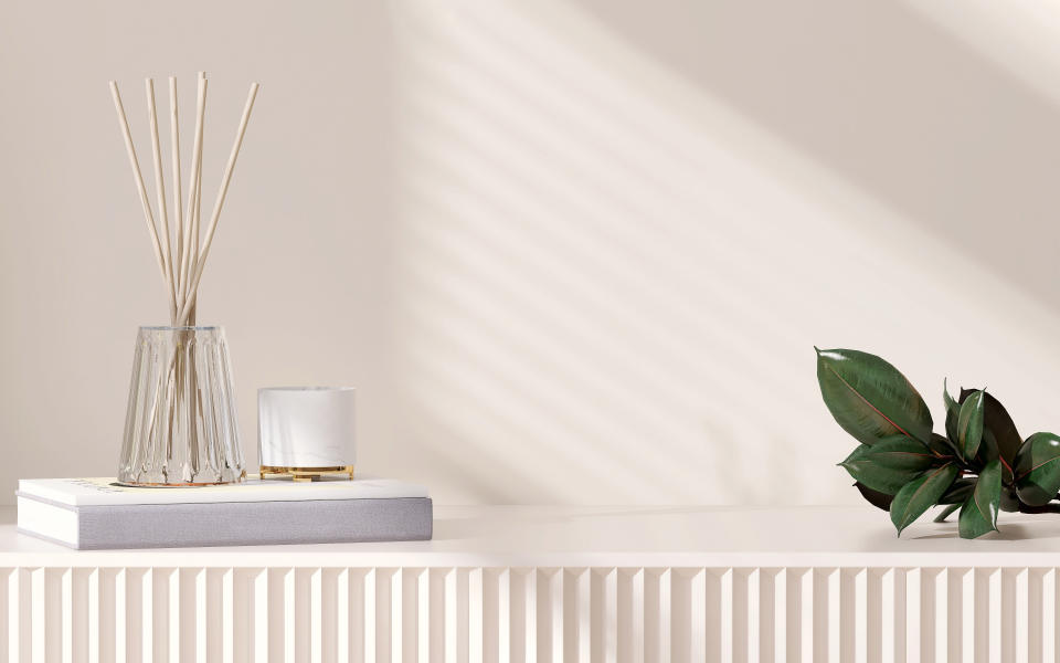 Empty space on beige cream cabinet with corrugated door, books, glass vase with reed diffuser, candle, green tropical tree leaf