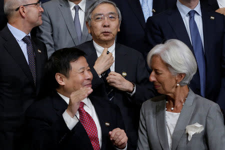 Bank of Japan (BOJ) Governor Haruhiko Kuroda (C) adjusts his tie behind International Monetary Fund (IMF) Managing Director Christine Lagarde (R) and Chinese Vice Finance Minister Zhu Guangyao at G-20 finance ministers and central bank governors family photo before a plenary session during the IMF/World Bank annual meetings in Washington, U.S., October 12, 2017. REUTERS/Yuri Gripas