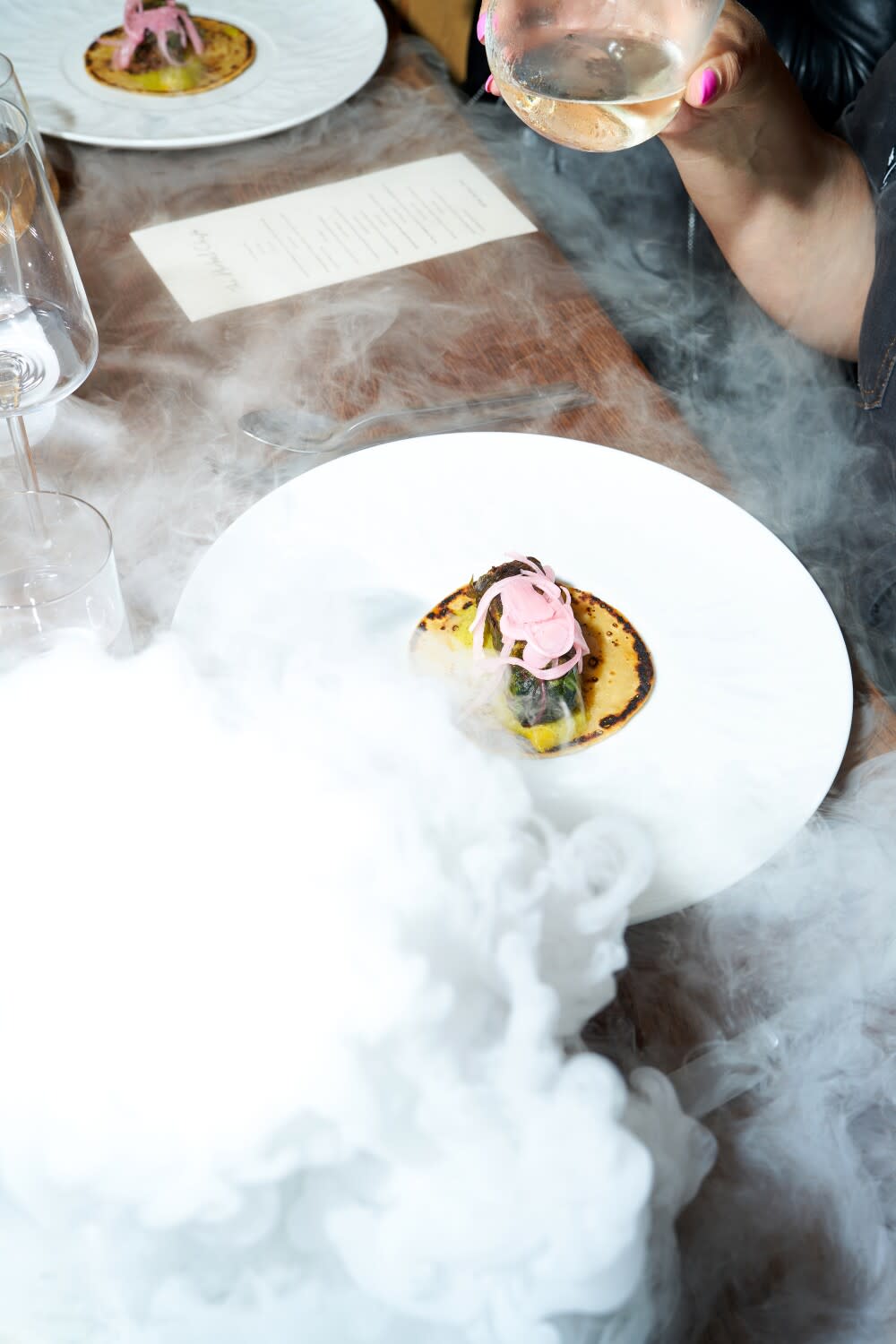 Smoke swirls around a plate containing a piece of meat atop a flatbread.