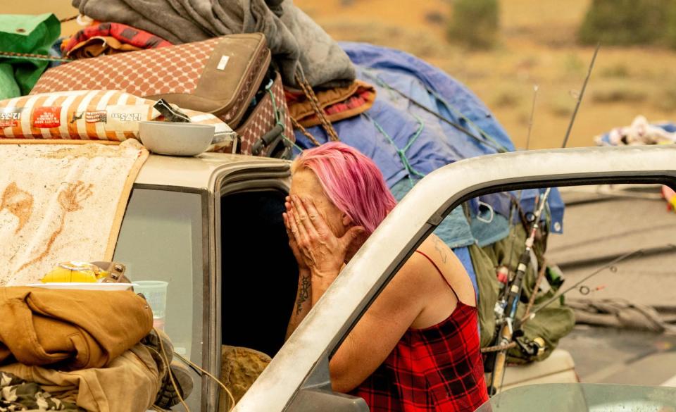 Regina Rutledge covers her face with both her hands outside her packed truck.