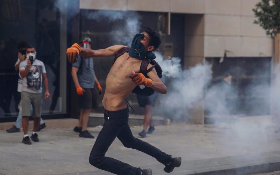 An anti-government protester throws a stone towards riot police during a protest near Parliament Square, in Beirut, Lebanon -  Hassan Ammar/ Hassan Ammar