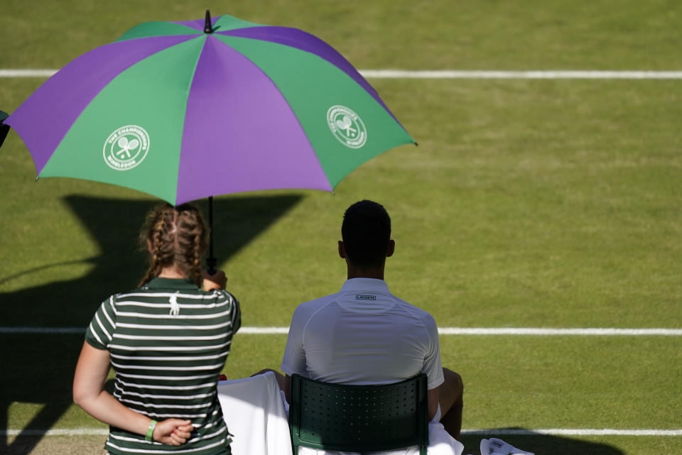 A ballgirl shields Serbia's Novak Djokovic from the sun during a change of ends break as he plays Britain's Cameron Norrie in a men's singles semifinal on day twelve of the Wimbledon tennis championships in London, Friday, July 8, 2022. (AP Photo/Gerald Herbert)