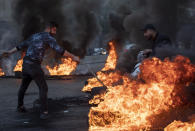 A man rides his scooter as an anti-government protester sets fire to tires to block a road, during a protest in Beirut, Lebanon, Tuesday, March 2, 2021. Scattered protests broke out in different parts of Lebanon Tuesday after the Lebanese pound hit a record low against the dollar on the black market, a sign of the country's multiple crises deepening with no prospects for a new Cabinet in the near future. (AP Photo/Hassan Ammar)