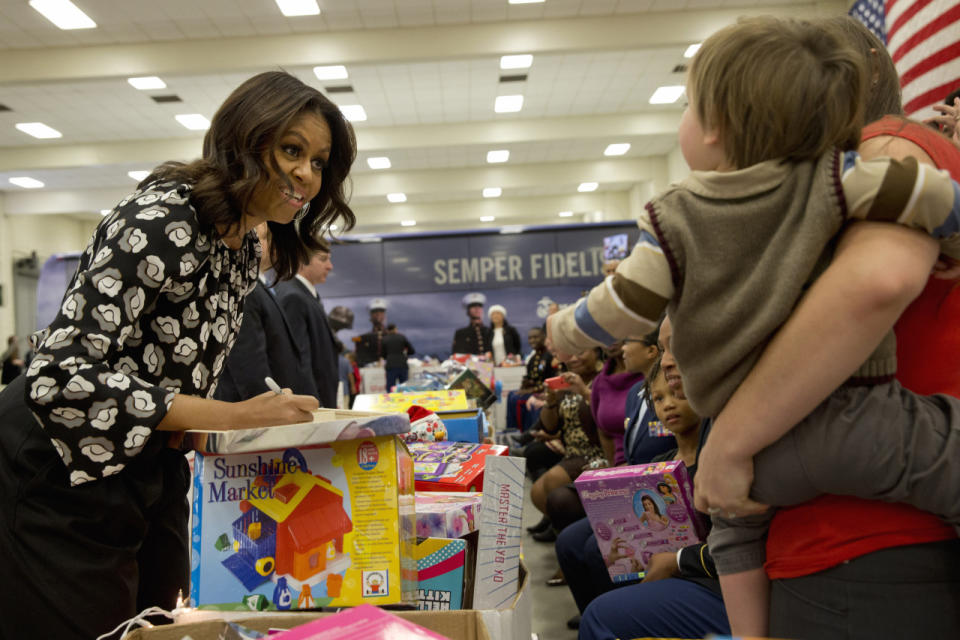 Michelle Obama in a black and white floral blouse paired with black pants helping out at a Toys for Tots event. 