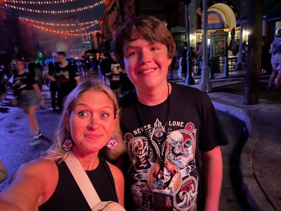 The author, left, and her son at Halloween Horror Nights. It is nighttime and they are lit up by bright lights, smiling and looking at the camera.