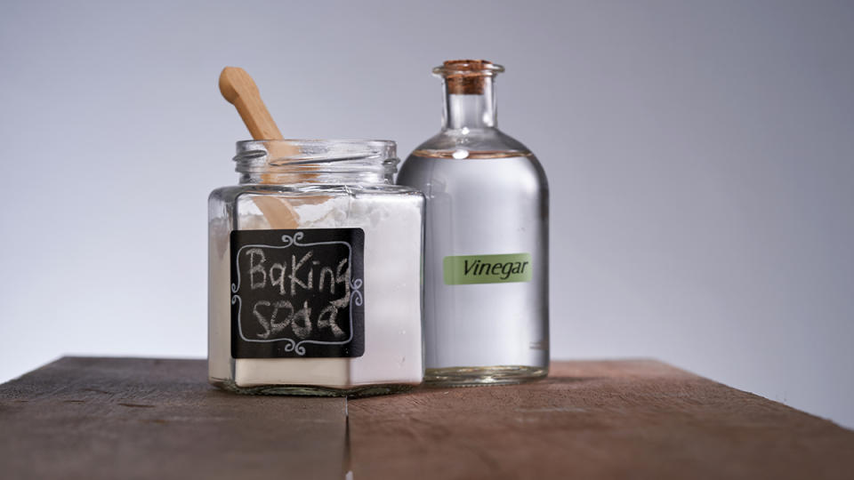 Wooden spoon inside a jar of baking soda next to a jar of vinegar 