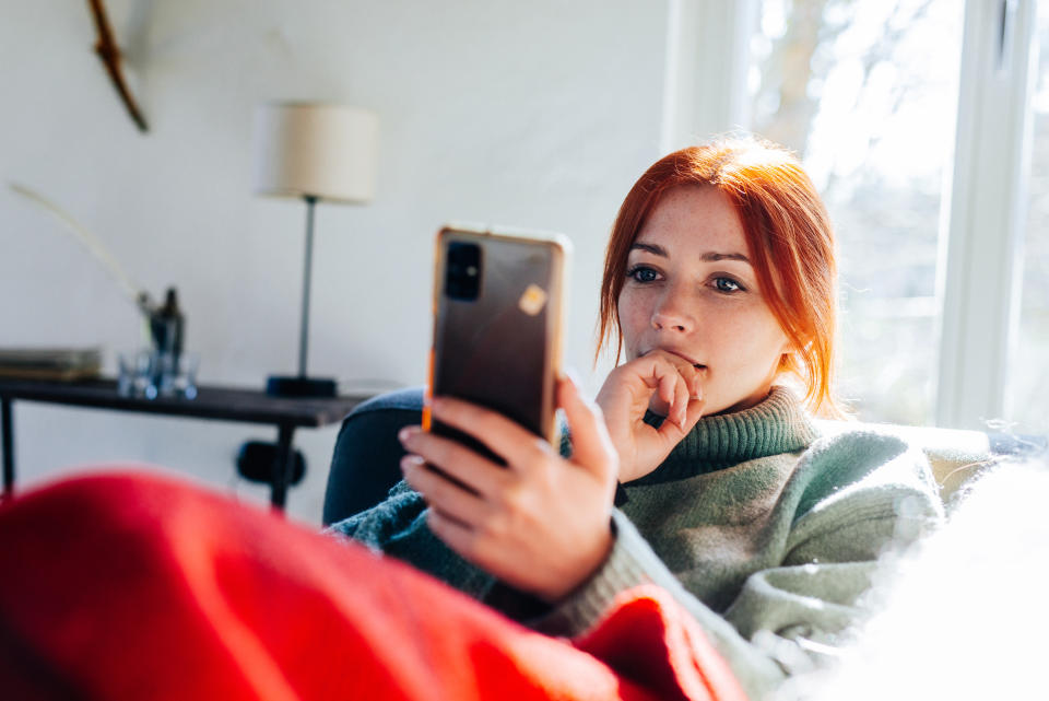 Woman with red hair looking on screen of her mobile phone.