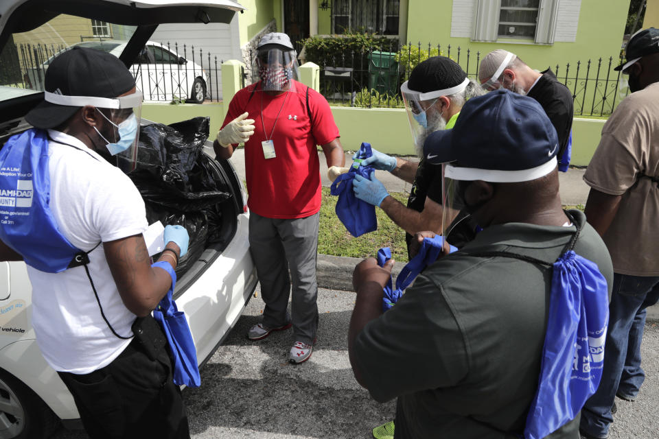 Morris Copeland, of the Strategic Urban Response to Guideline Education (SURGE) group, center, passes out kits to team members which they will distribute to residents living in COVID-19 hotspots, during the new coronavirus pandemic, Wednesday, July 1, 2020, in the Liberty City neighborhood of Miami. The teams were formed by Miami-Dade County to help flatten the curve of the coronavirus. The kits contain masks, hand sanitizer, and information about testing locations. (AP Photo/Lynne Sladky)