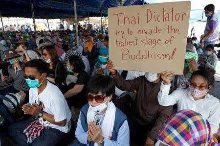 Thai worshippers hold a placard as others pray at the gate of Dhammakaya temple, after police ordered thousands of worshippers to leave the temple so it can search for its former abbot, in Pathum Thani province, Thailand February 19, 2017. REUTERS/Chaiwat Subprasom