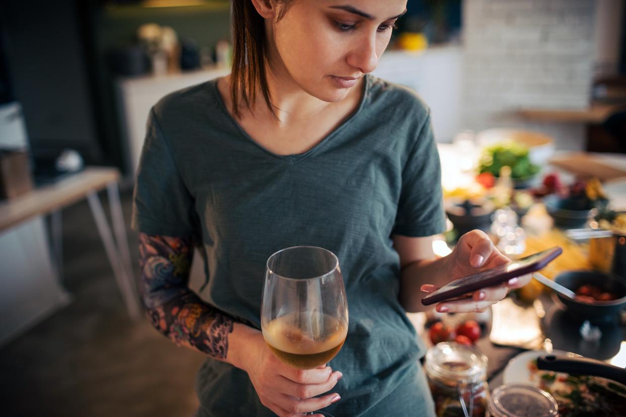 woman holding wine and using smart phone while preparing a food