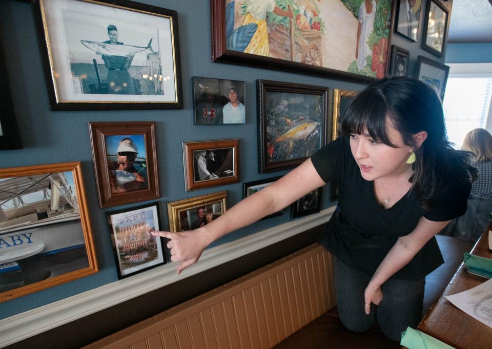 Server Haley Jennette points out photos of their annual staff fishing trip on display at Dharma Blue in downtown Pensacola on Friday, April 12, 2024.