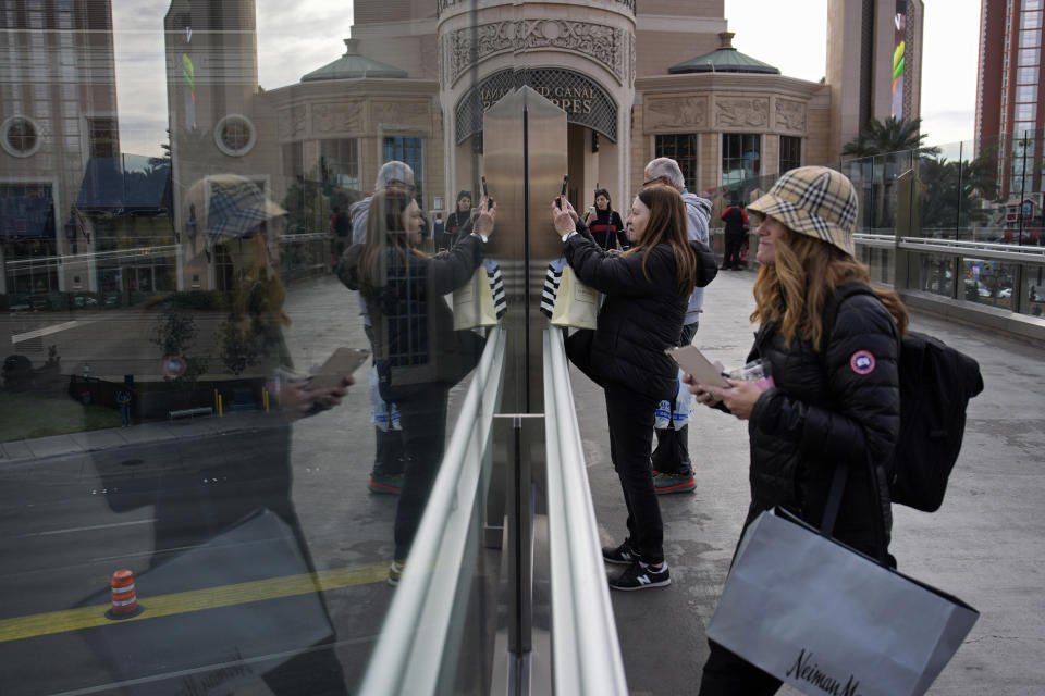 People stop to take pictures on a pedestrian bridge along the Las Vegas Strip, Wednesday, Jan. 17, 2024, in Las Vegas. Stopping or standing is prohibited on Las Vegas Strip pedestrian bridges after a new ordinance took effect Tuesday, Jan. 17, 2024. (AP Photo/John Locher)