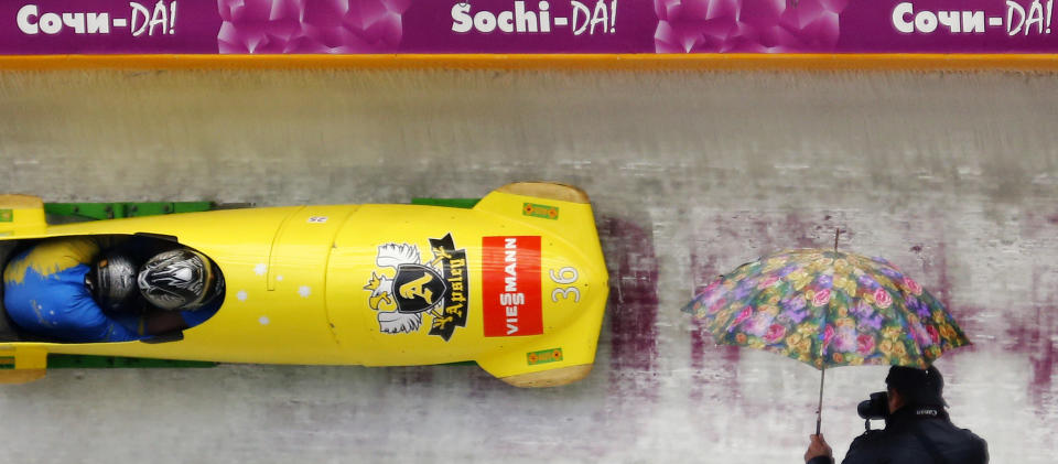 A spectator holding an umbrella takes photographs during the two-men bobsleigh test event at the "Sanki" sliding center in Rosa Khutor, a venue for the Sochi 2014 Winter Olympics near Sochi February 16, 2013. Although many complexes and venues in the Black Sea resort of Sochi mostly resemble building sites that are still under construction, there is nothing to suggest any concern over readiness. Construction will be completed by August 2013 according to organizers. The Sochi 2014 Winter Olympics opens on February 7, 2014. REUTERS/Kai Pfaffenbach (RUSSIA - Tags: BUSINESS CONSTRUCTION CITYSCAPE ENVIRONMENT SPORT OLYMPICS BOBSLEIGH TPX IMAGES OF THE DAY) - RTR3DV4U