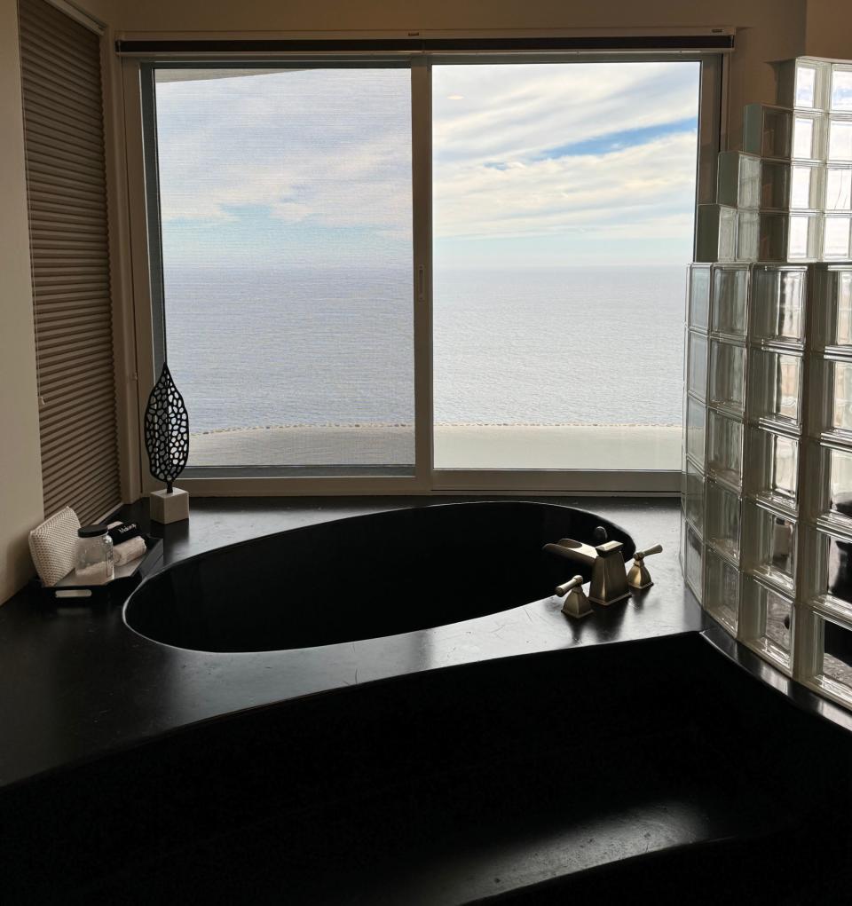 A luxurious bathroom with an ocean view features a sunken black bathtub, modern fixtures, and large windows offering a stunning scenic vista