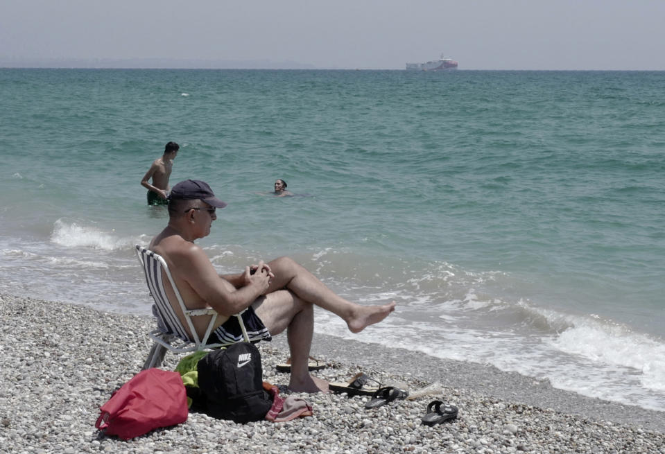 In this photo taken Monday, July 27, 2020, people relax on the beach with a view of the Turkey's research vessel, Oruc Reis, in the background, anchored off the coast of Antalya on the Mediterranean, Turkey. A top Turkish official said Tuesday that Turkey will suspend research for oil and gas exploration in disputed waters in the Eastern Mediterranean. President Recep Tayyip Erdogan told his aides to "be constructive and put this on hold for some time," presidential spokesman Ibrahim Kalin told Turkish broadcaster CNN Turk. (AP Photo/Burhan Ozbilici)