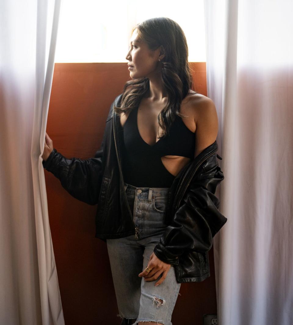 Julia Lee poses for a portrait, standing by a window, partially pulling a curtain away as she looks out.