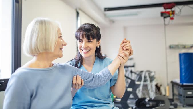 Nurse assisting senior woman with hand exercise.