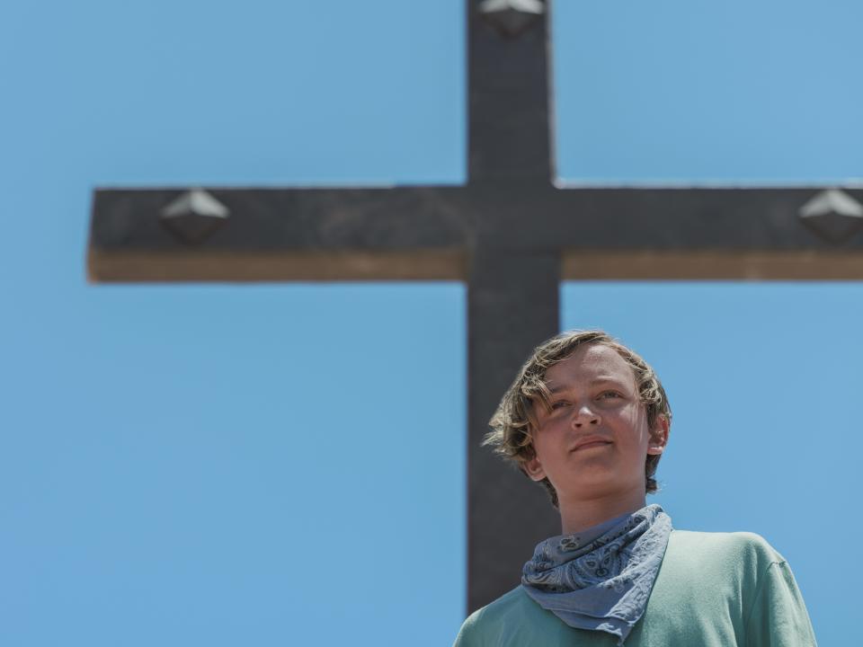 jodie in the chosen one, a preteen boy standing in front of a large cross 