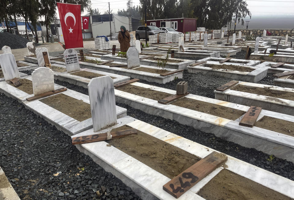 A woman stands next to a grave in a cemetery where some of the victims of the powerful Feb. 6, 2023 earthquake are buried in Antakya, southern Turkey, Friday, Jan. 12, 2024. A year after the earthquake struck, some families are still searching for missing loved ones. (AP Photo/Khalil Hamra)