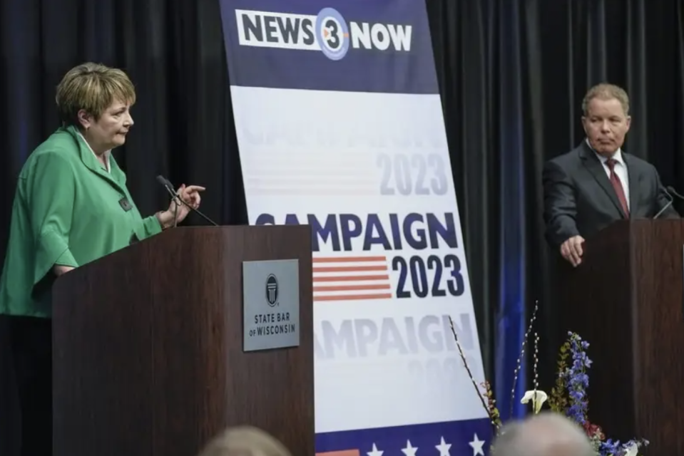 Dan Kelly and Janet Protasiewicz debate each other onstage in between a giant sign that reads "campaign 2023"