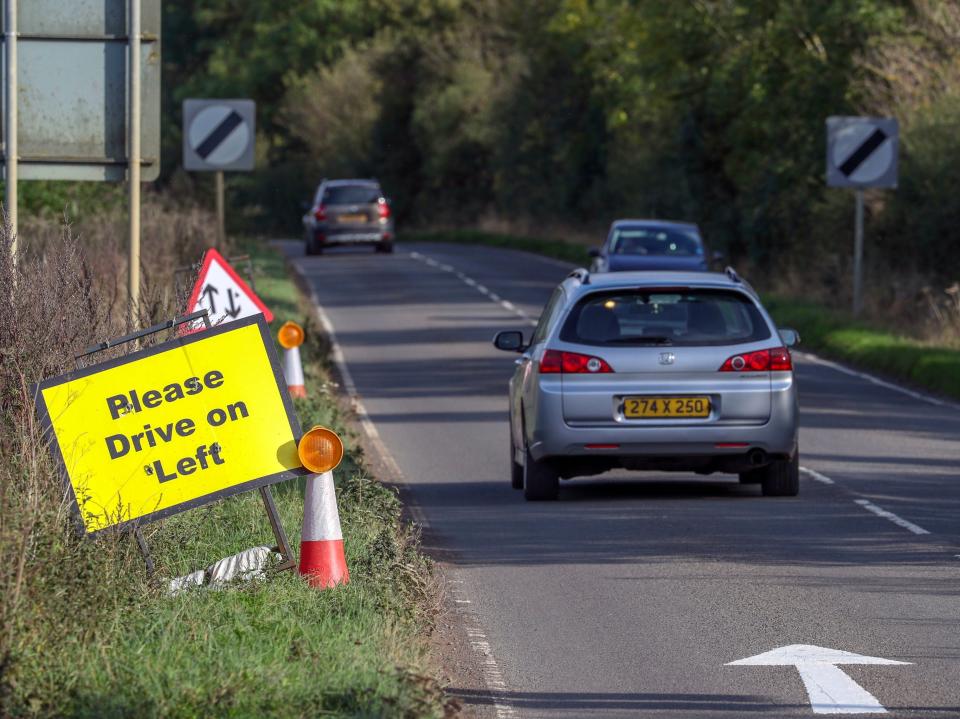 A vehicle with diplomatic plates passes a Please Drive on Left sign and road marking that have been placed on the B4031 outside RAF Croughton, where Harry Dunn diedPA