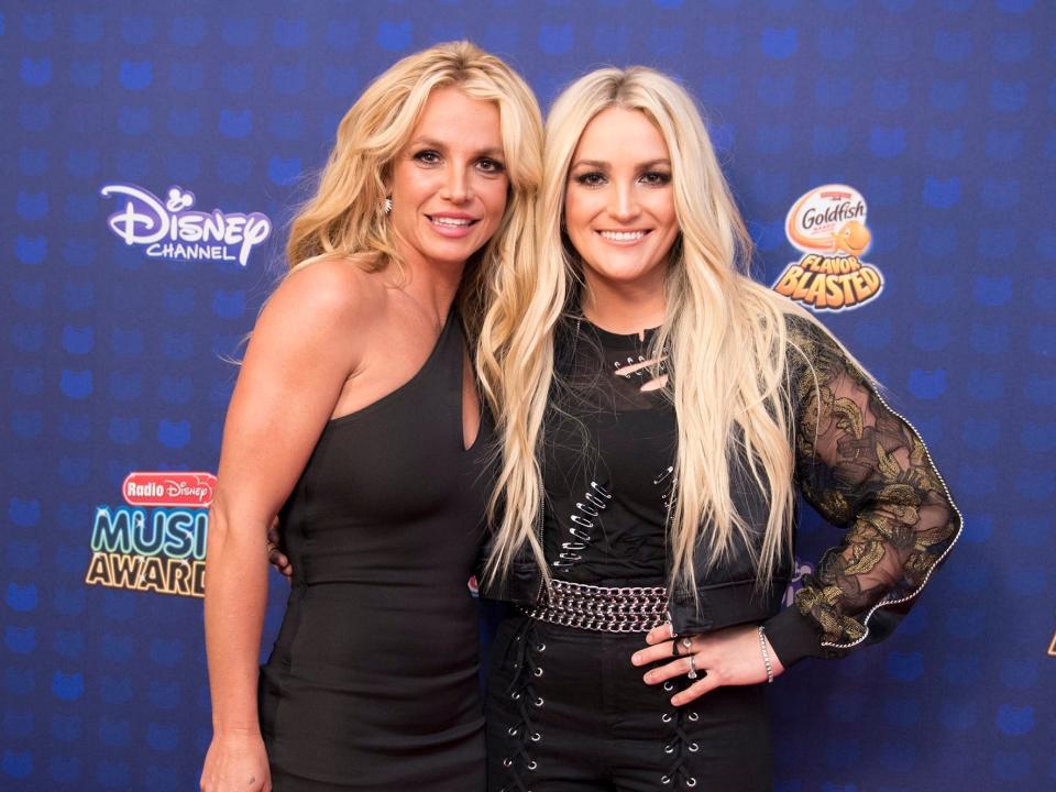 Britney and Jamie Lynn in black ensembles in front of a Disney backdrop.