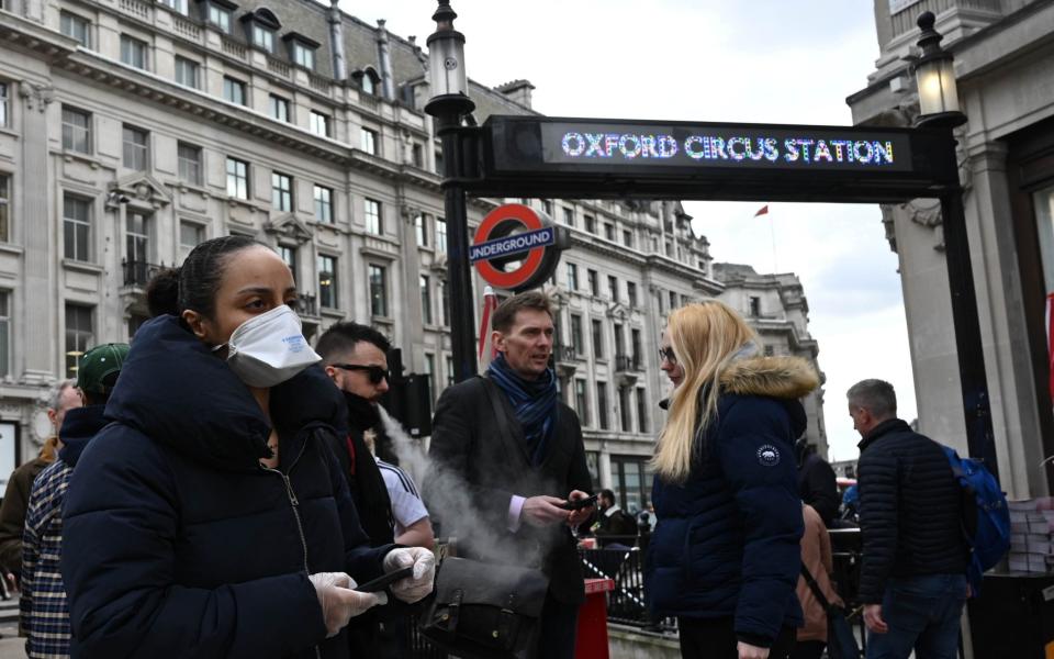 A woman wearing a protective mask and gloves walks through Oxford Circus in London - Neil Hall/Shutterstock