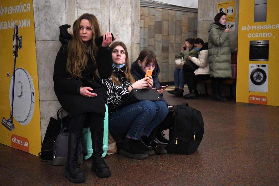 Girls hold their mobile phone as they take refuge in a metro station in Kyiv in the morning of February 24, 2022. Air raid sirens rang out in downtown Kyiv today as cities across Ukraine were hit with what Ukrainian officials said were Russian missile strikes and artillery. - Russian President Vladimir Putin announced a military operation in Ukraine on Thursday with explosions heard soon after across the country and its foreign minister warning a 