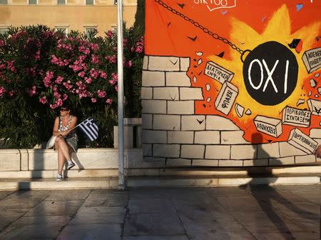 A woman sits near a mural depicting a wrecking ball smashing a wall of austerity measures in Athens, July 22, 2015. REUTERS/Alkis Konstantinidis