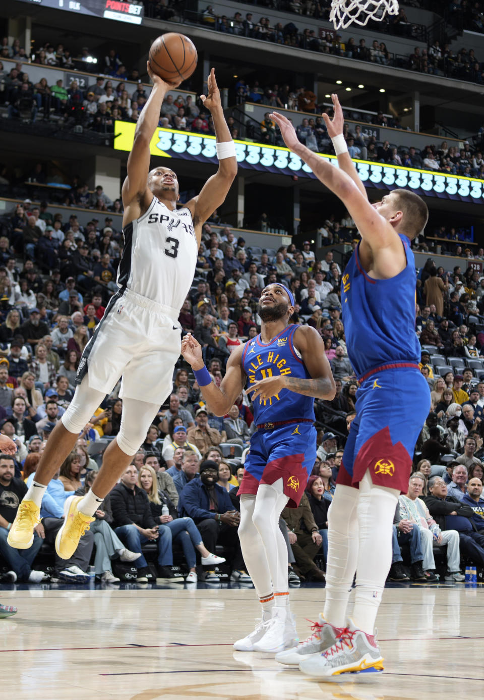 San Antonio Spurs forward Keldon Johnson, left, drives to the basket as Denver Nuggets forward Bruce Brown, center, and center Nikola Jokic defend in the first half of an NBA basketball game Saturday, Nov. 5, 2022, in Denver. (AP Photo/David Zalubowski)