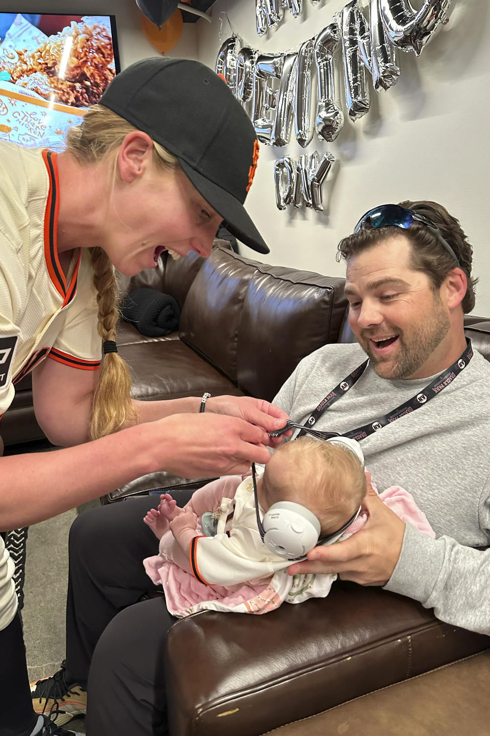 San Francisco Giants major league assistant coach Alyssa Nakken, left, puts noise reduction headphones on her daughter, Austyn, as her husband, Robert, watches before a baseball game between the Giants and the San Diego Padres in San Francisco, Friday, April 5, 2024. (AP Photo/Janie McCauley)