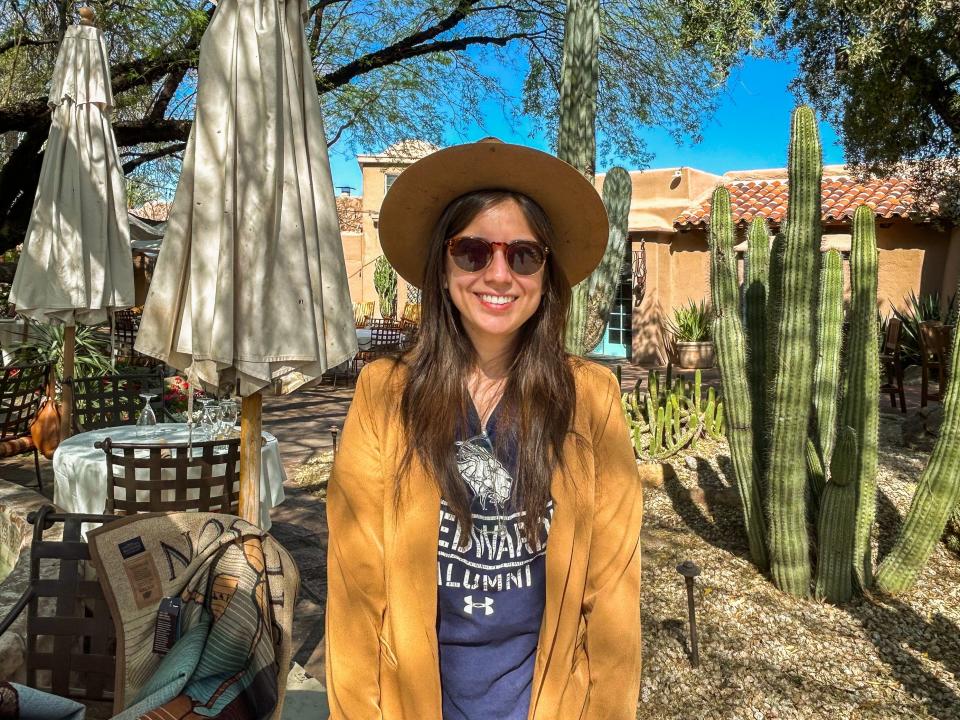 The author in a cowboy hat and sunglasses stands smiling in front of cacti and an adobe building in Scottsdale