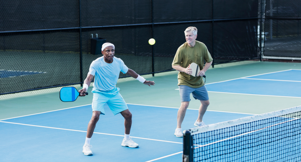 two elderly men playing pickleball on court outside 
