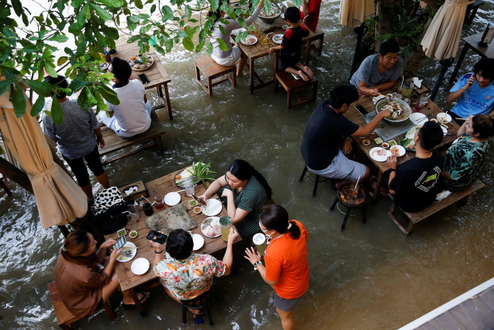 People eat food at a flooded restaurant, where patrons stand up from their tables every time the waves come in, on a river bank in Nonthaburi near Bangkok, Thailand, October 7, 2021. REUTERS/Soe Zeya Tun